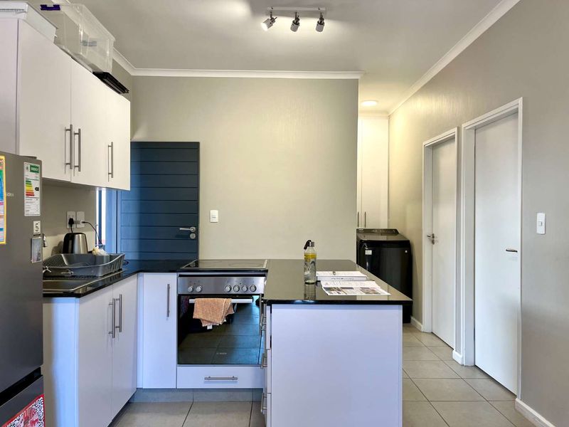 Modern kitchen featuring white cabinetry, black granite countertops, built-in oven and hob, and tiled flooring with adjacent laundry area access.