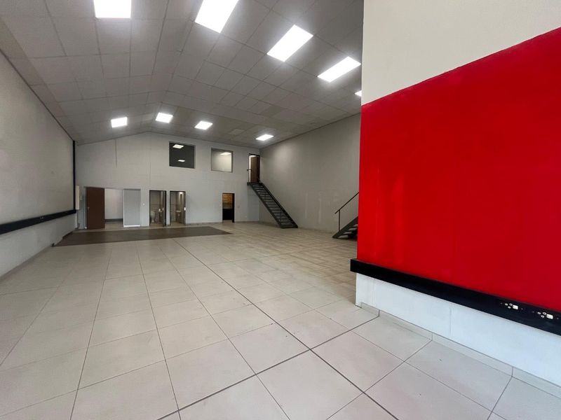 Spacious open-plan commercial unit featuring tiled flooring, suspended ceilings with recessed lighting, and an internal metal staircase leading to an upper level.
