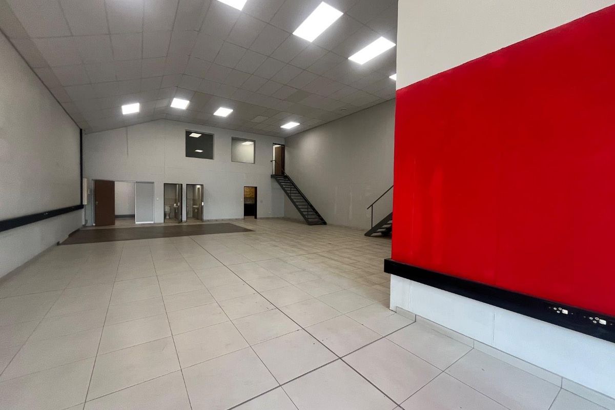 Spacious open-plan commercial unit featuring tiled flooring, suspended ceilings with recessed lighting, and an internal metal staircase leading to an upper level.