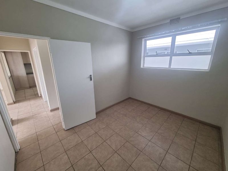 A clean, empty bedroom featuring neutral wall tones, tiled flooring, and a frosted glass window providing natural light.