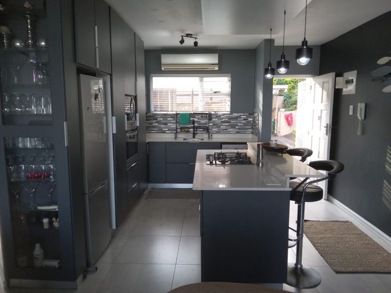 Modern kitchen featuring dark cabinetry, a central island with a gas cooktop, tiled backsplash, and integrated appliances, leading out to an exterior area.