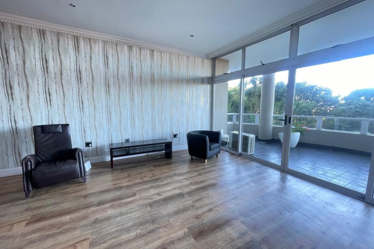 Spacious living area featuring laminate flooring, textured wallpaper, and large sliding glass doors providing access to an outdoor balcony.