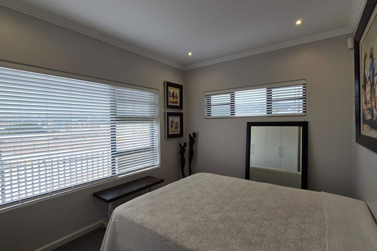 A well-maintained bedroom featuring neutral walls, recessed ceiling lighting, and large windows fitted with horizontal blinds.