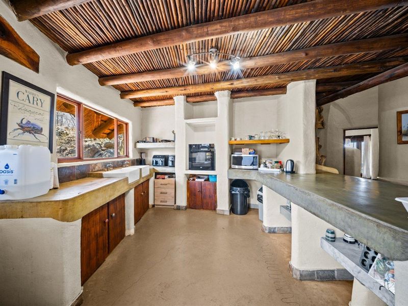 Rustic kitchen featuring exposed timber beam ceilings, built-in concrete countertops, and a double farmhouse sink with wooden cabinetry.