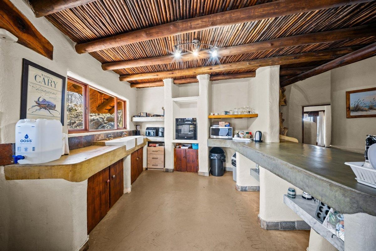 Rustic kitchen featuring exposed timber beam ceilings, built-in concrete countertops, and a double farmhouse sink with wooden cabinetry.