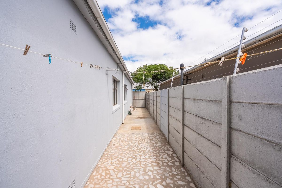 A narrow side passage featuring a paved walkway, precast concrete boundary wall, and installed electric fencing.