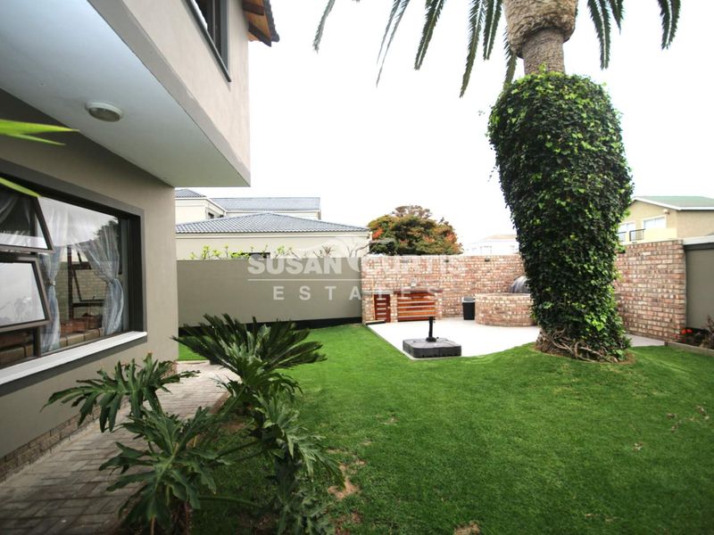 Rear garden featuring a lawn, paved patio area with a built-in braai, and a brick boundary wall.