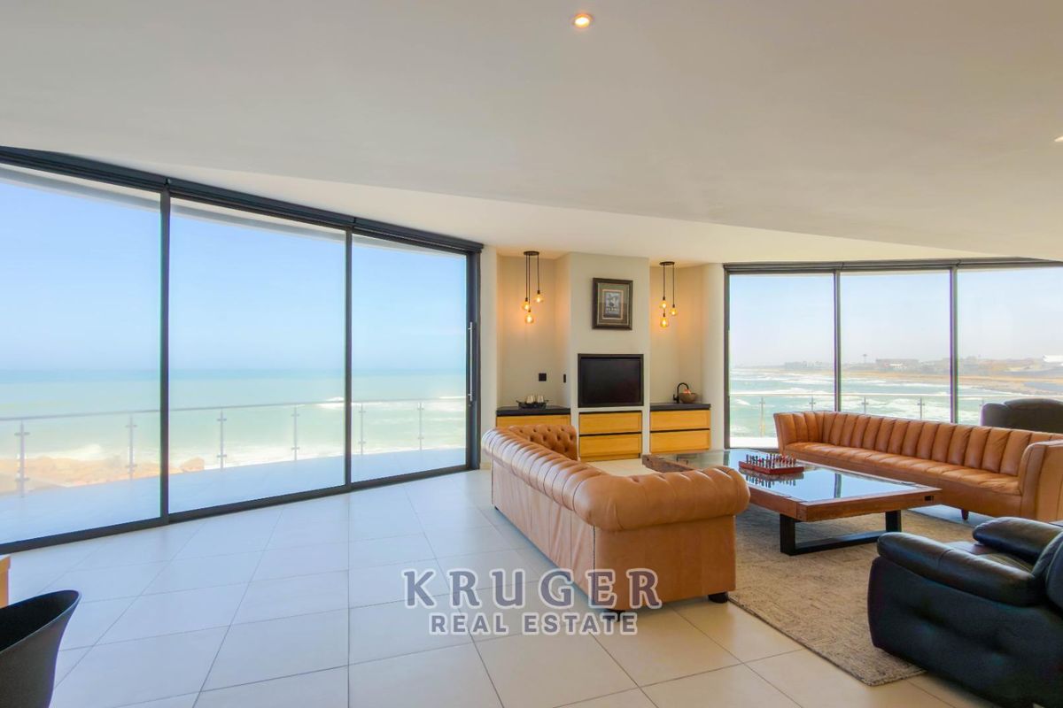 Spacious open-plan living area featuring floor-to-ceiling glass doors with panoramic ocean views, modern tiled flooring, and a built-in media unit.