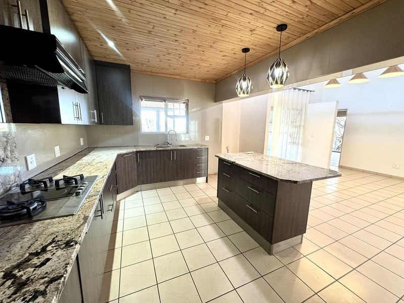 Modern kitchen featuring dark cabinetry, granite countertops, a central island, gas hob, and a distinctive timber-clad ceiling with tiled flooring.