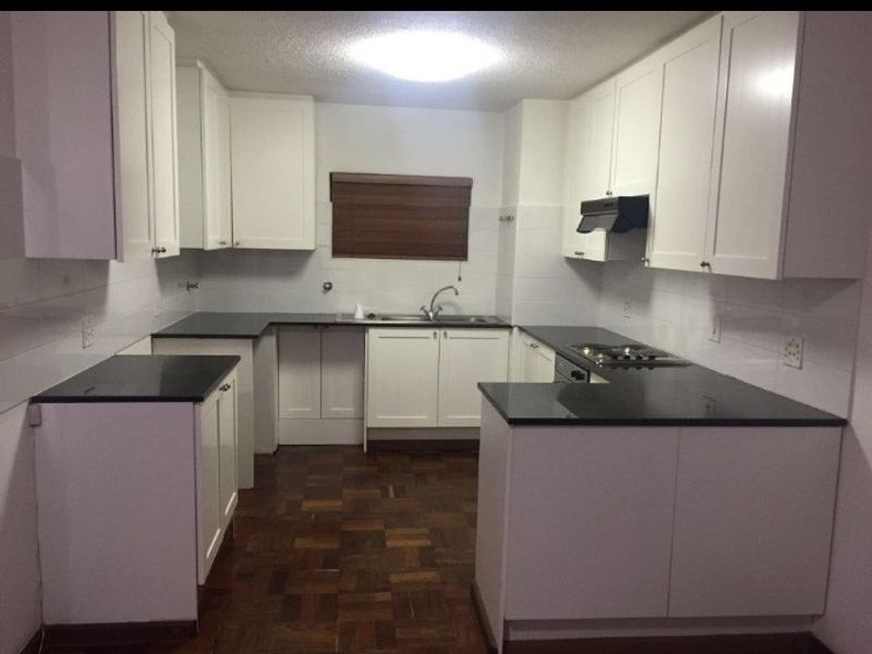 A clean, functional kitchen featuring white cabinetry, dark granite countertops, built-in hob, extractor fan, and classic parquet flooring.