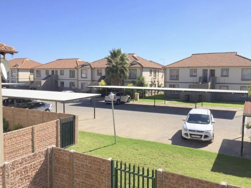 Exterior view of the apartment complex featuring paved parking areas with covered carports, brick boundary walls, and well-maintained communal garden spaces.
