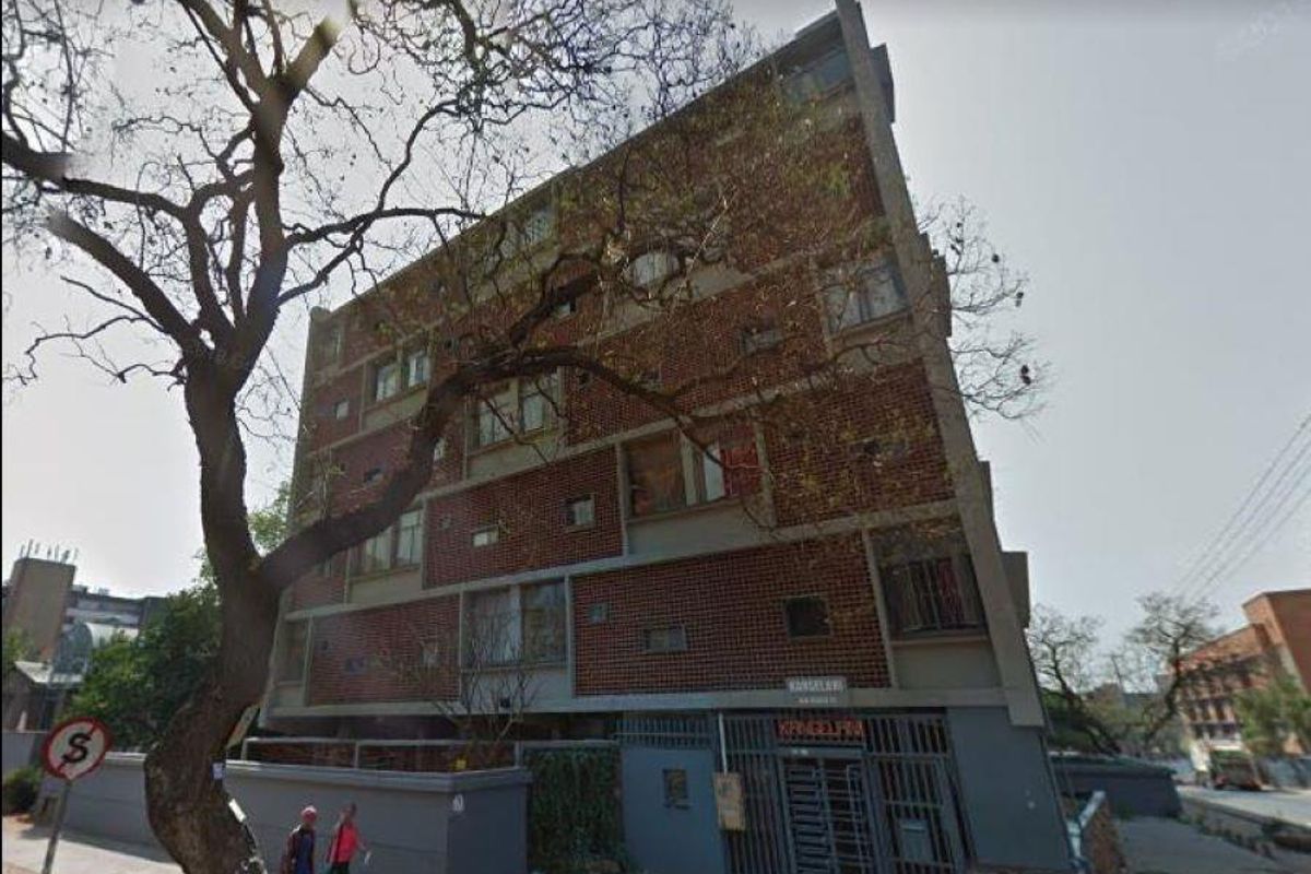 Exterior view of a multi-story apartment building featuring a brick facade, concrete structural elements, and a secure gated entrance.