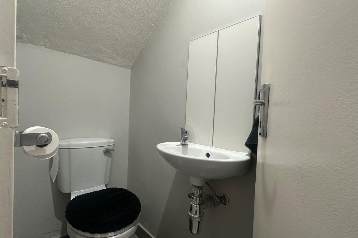 Compact guest bathroom featuring a wall-mounted basin, mirrored cabinet, and standard toilet, situated under a sloped ceiling.