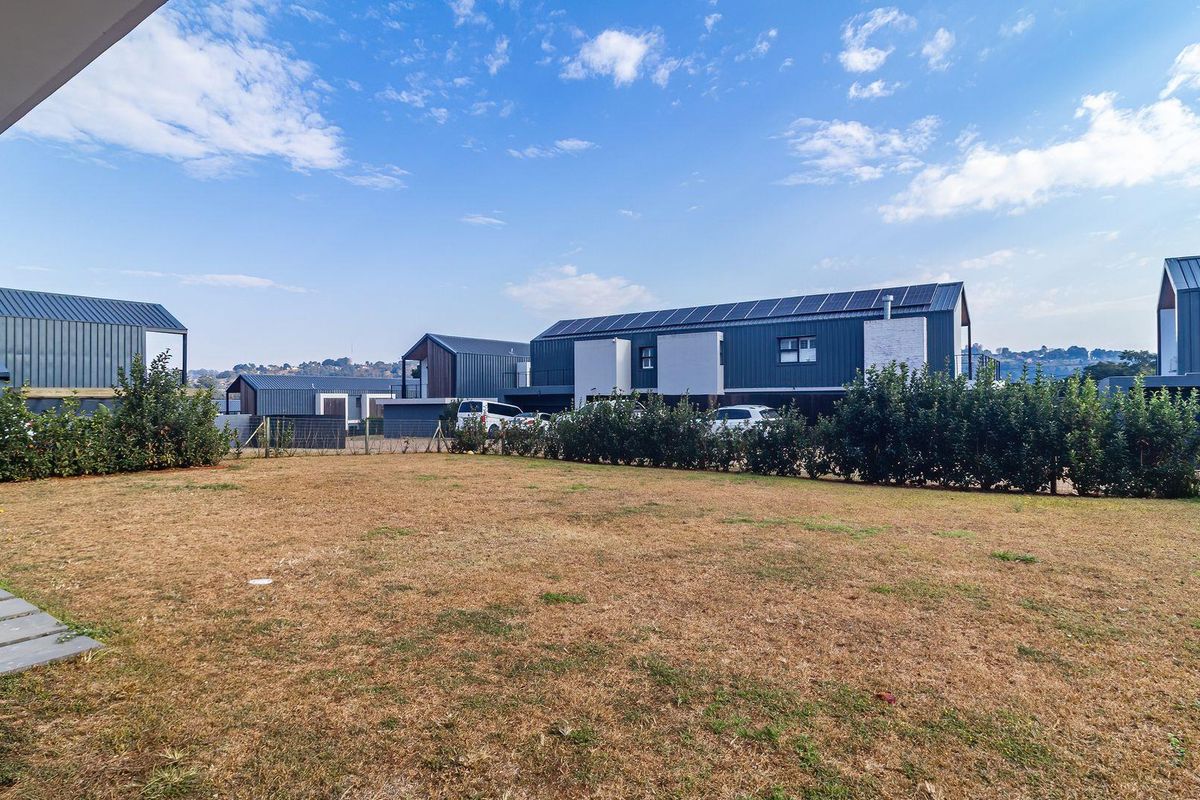 A view of the rear garden area featuring a lawn and established hedge, with modern residential buildings in the background.