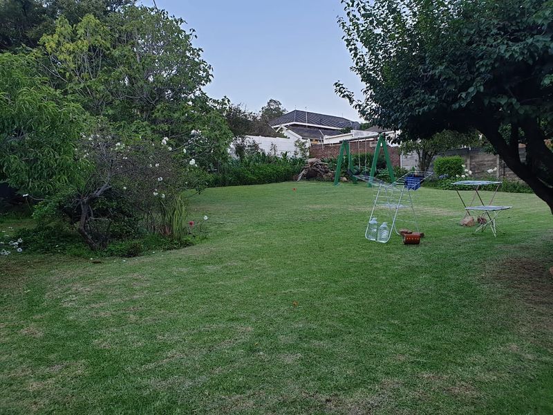 A spacious, well-maintained residential garden featuring a large lawn, mature trees, and perimeter boundary walls.