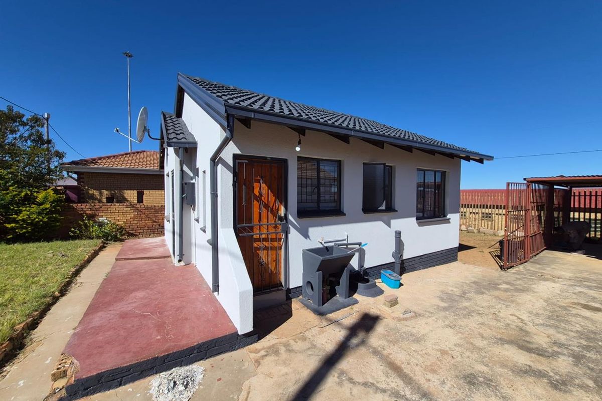 A well-maintained exterior view of a small residential dwelling featuring a tiled roof, security gate, and an external utility sink.