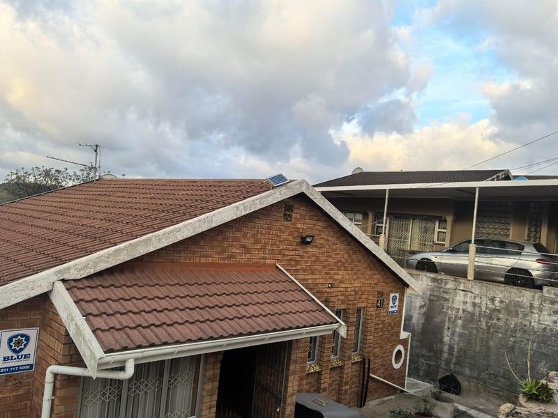 Front elevation of a brick house featuring a tiled roof, solar panel, and security gate, showing standard residential wear.