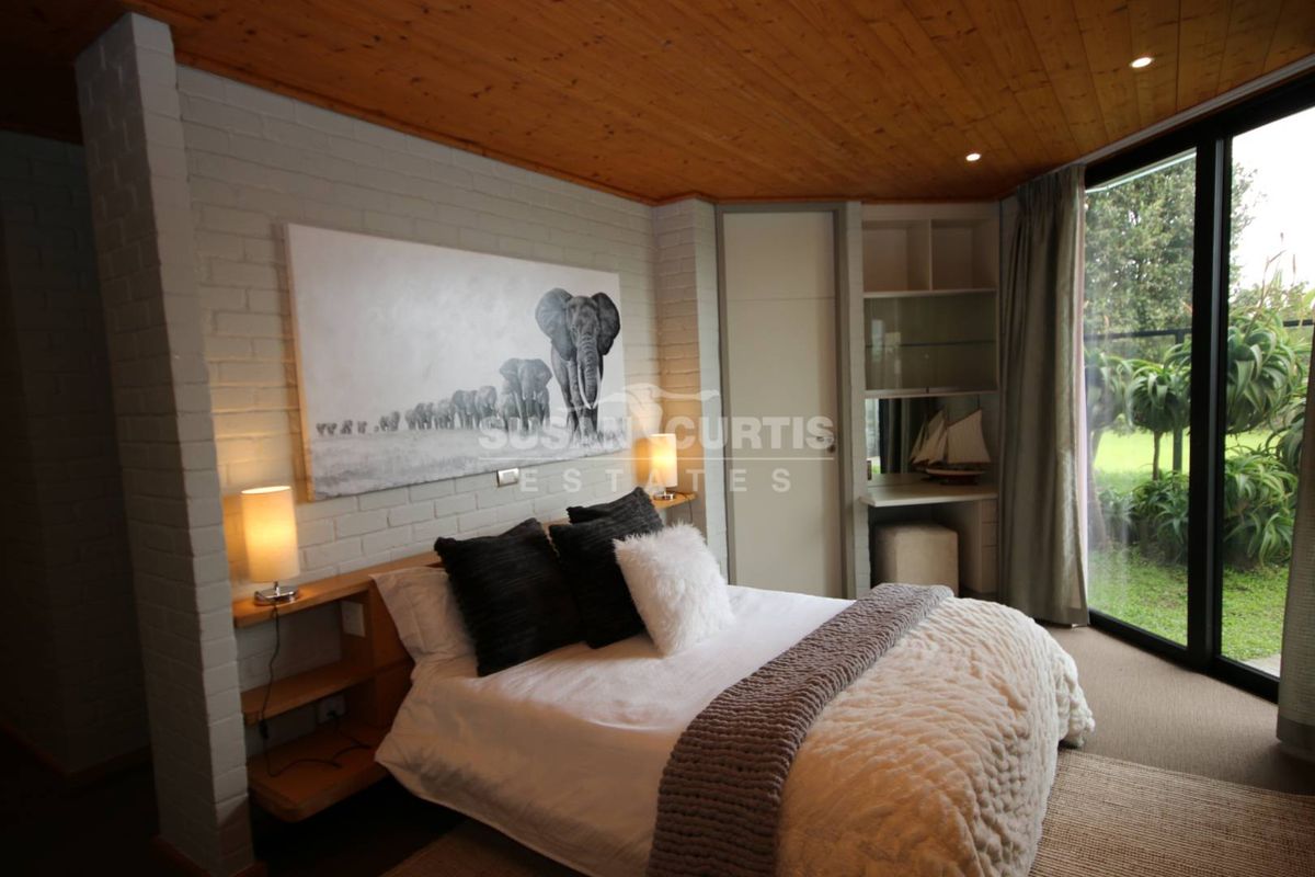 A well-maintained bedroom featuring a timber ceiling, painted brick wall, built-in desk and shelving, and large sliding glass doors with garden access.