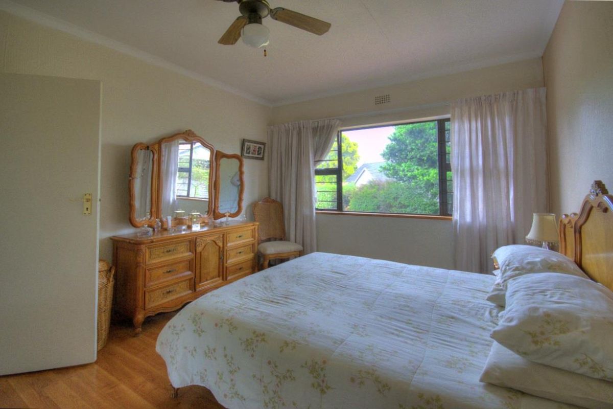 A well-lit bedroom featuring timber flooring, a ceiling fan, and a large window overlooking the garden.