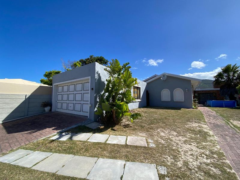 Front view of a single-story house featuring a single garage, paved driveway, and arched windows set within a residential garden.