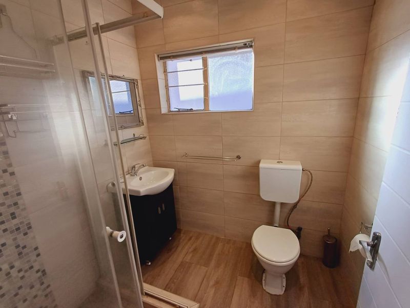 A modern bathroom featuring a glass shower enclosure, vanity cabinet with basin, and toilet, finished with neutral wall and floor tiles.