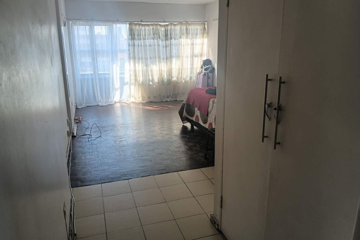 Bedroom featuring a combination of tiled and parquet flooring with a built-in cupboard, offering a functional space with potential for cosmetic updates.