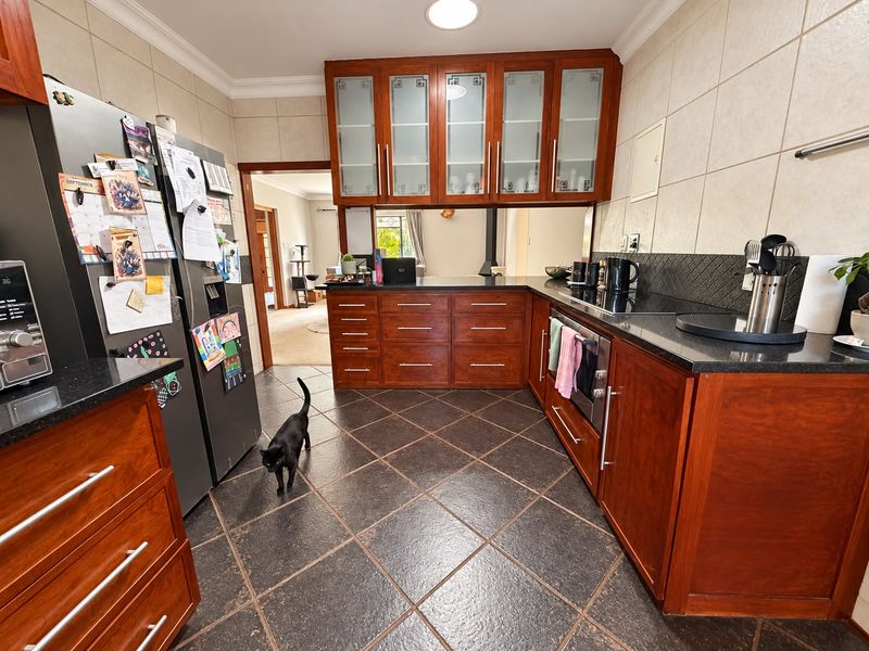 A well-maintained kitchen featuring rich wood cabinetry, granite countertops, glass-fronted display cabinets, and durable tiled flooring with a functional layout.