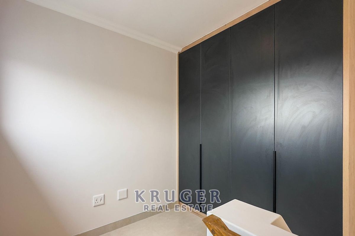 A clean, empty bedroom featuring modern dark built-in cupboards with sleek handles and neutral tiled flooring.