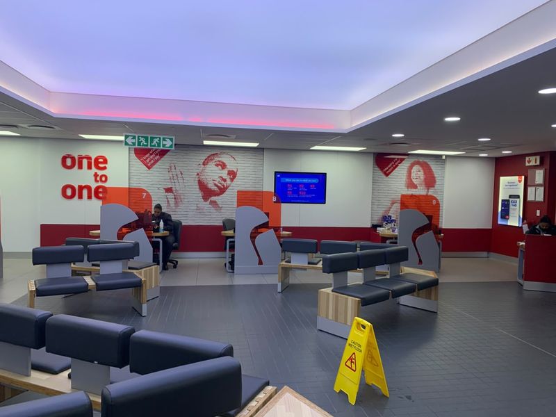 A modern retail banking or service interior featuring professional service counters, recessed ceiling lighting, and a spacious waiting area with fixed seating.