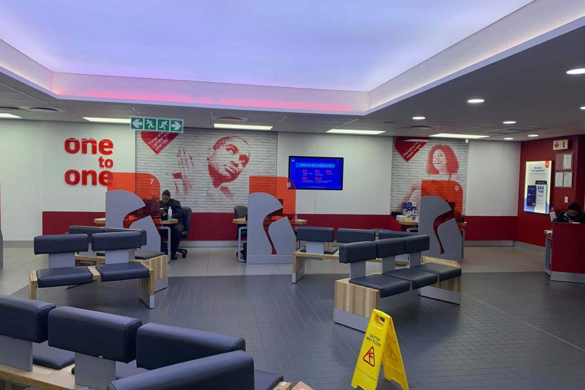 A modern retail banking or service interior featuring professional service counters, recessed ceiling lighting, and a spacious waiting area with fixed seating.
