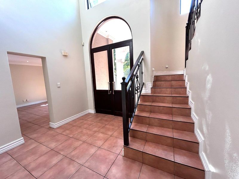 Spacious double-volume entrance hall featuring an arched front door, tiled flooring, and a staircase with decorative wrought iron railings.