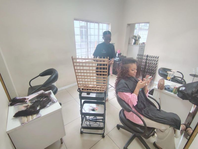 A functional office space featuring tiled flooring and a large window with security bars, currently utilized as a salon.