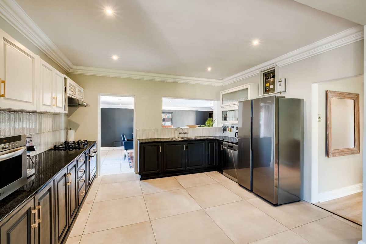 Modern kitchen featuring contrasting black and white cabinetry, granite countertops, integrated appliances, and large format floor tiles.