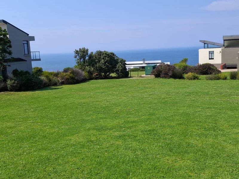 A well-maintained grassy garden area situated between residential properties, offering expansive views of the ocean.