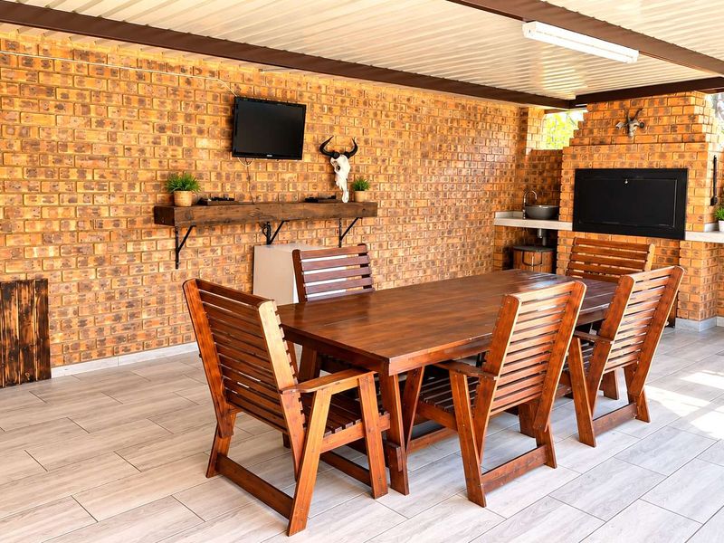 Covered outdoor patio featuring exposed brick walls, a built-in braai, prep sink, and modern tiled flooring, ideal for alfresco dining and entertaining.