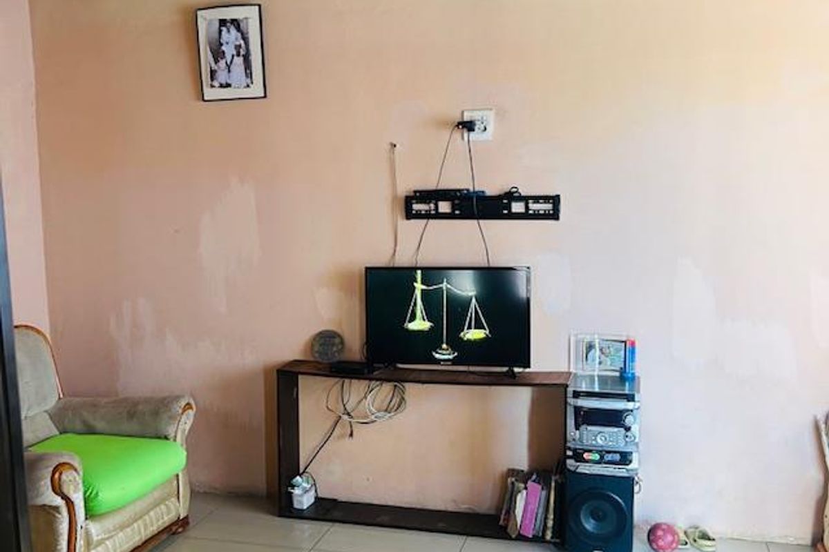 A living room area featuring tiled flooring and an exposed corrugated metal ceiling, requiring cosmetic updates to the wall finishes.