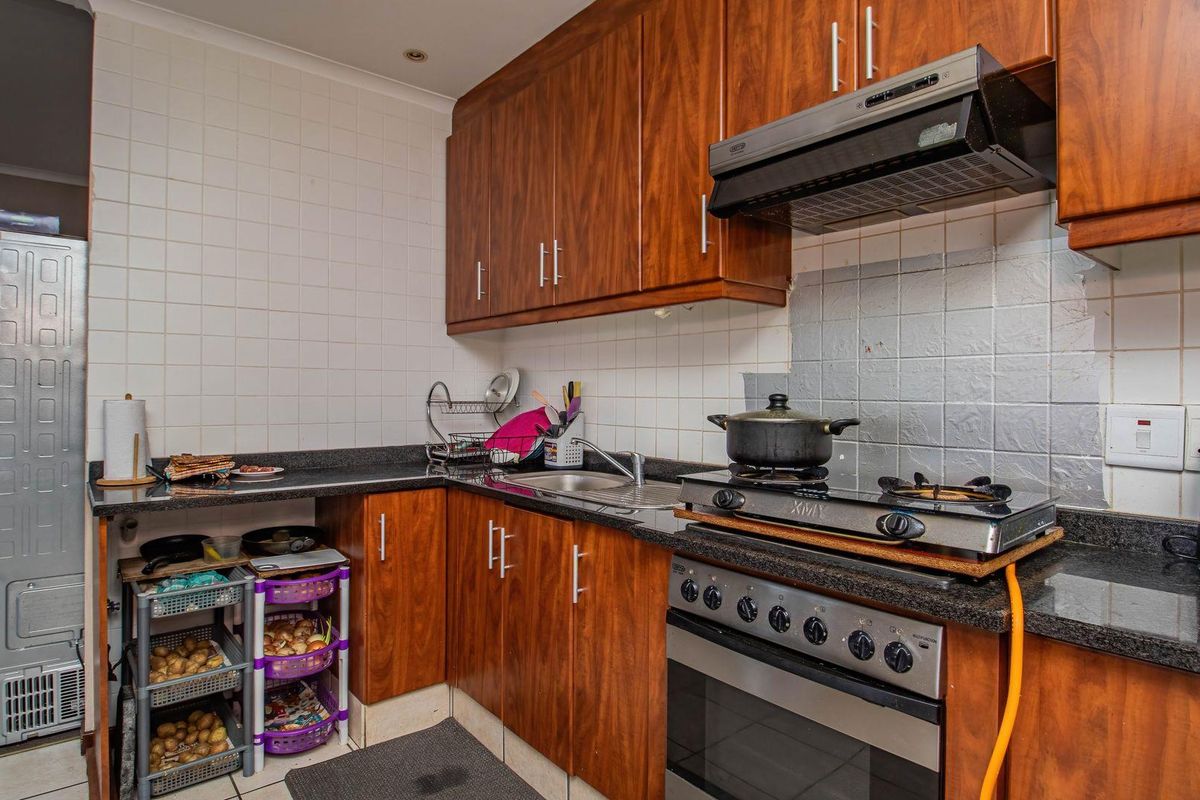 A functional kitchen featuring wood-finish cabinetry, granite countertops, a built-in oven, and a gas hob with an extractor fan.