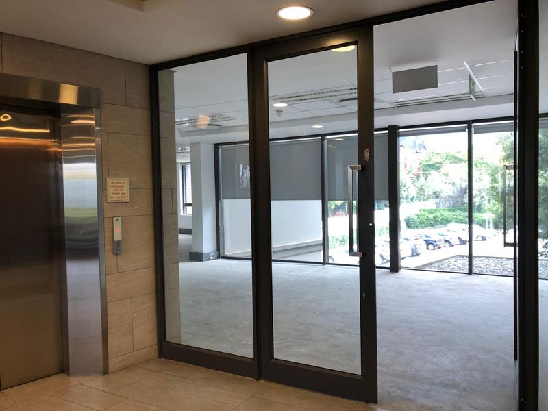 A bright, vacant office space featuring floor-to-ceiling windows, modern glass partitioning, and direct access to a stainless steel elevator lobby.