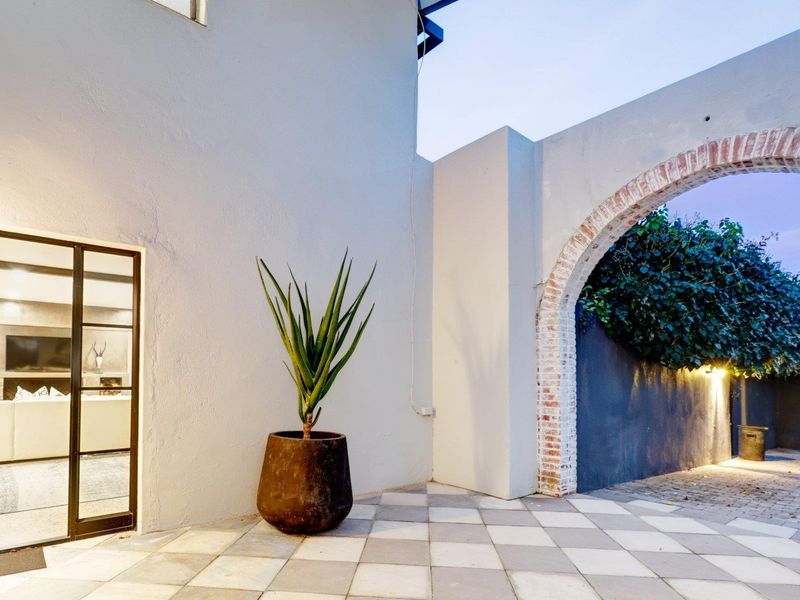 A charming outdoor patio area featuring a classic brick archway, tiled flooring, and direct access to the interior living space through a steel-framed glass door.