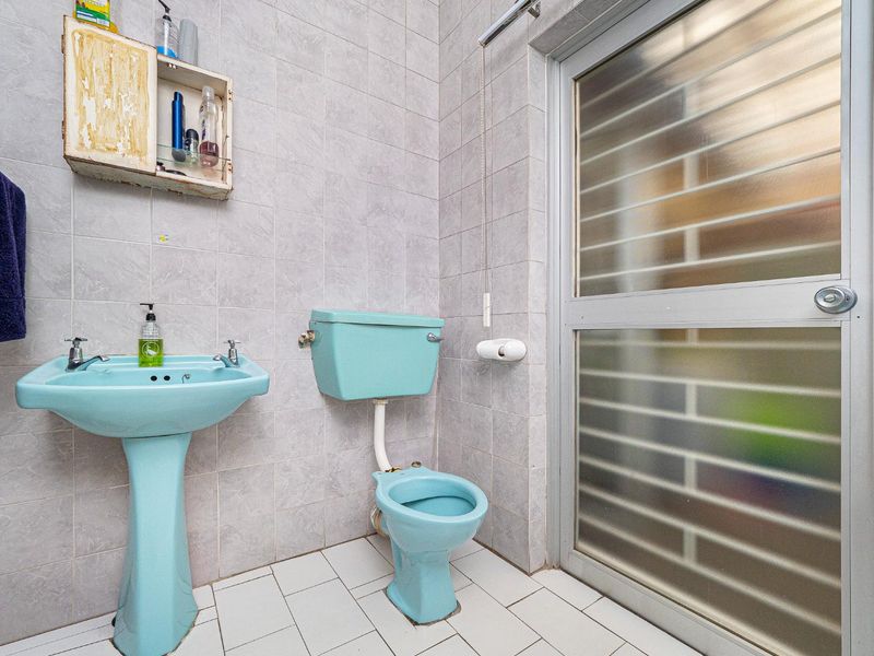 A dated bathroom featuring original blue sanitaryware, full-height wall tiling, and a frosted glass door.