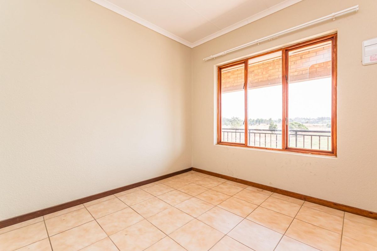A bright, empty bedroom featuring tiled flooring, wooden window frames, and neutral walls, offering a blank canvas for personalization.