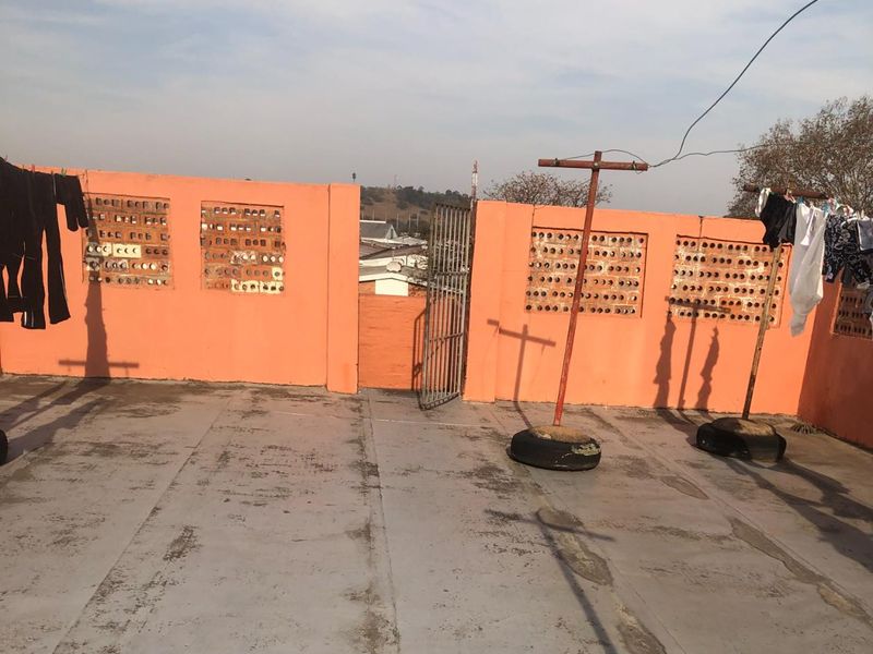 An open-air rooftop patio featuring a masonry perimeter wall with decorative brick ventilation blocks and a metal security gate.
