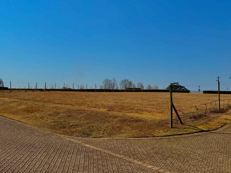 A vacant residential plot featuring a paved driveway entrance and perimeter wire fencing, offering a clear, level space ready for development.