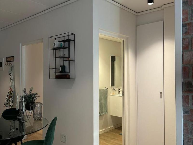 A well-lit hallway featuring laminate flooring, modern recessed spotlights, and a built-in storage cupboard, providing access to adjacent rooms.