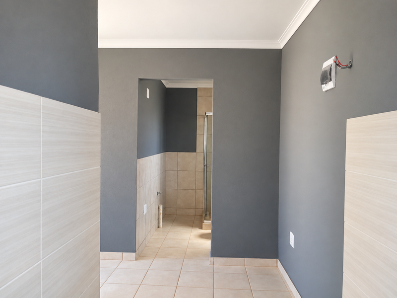 A clean, empty bathroom space featuring neutral wall and floor tiling, a shower enclosure, and modern grey painted walls.