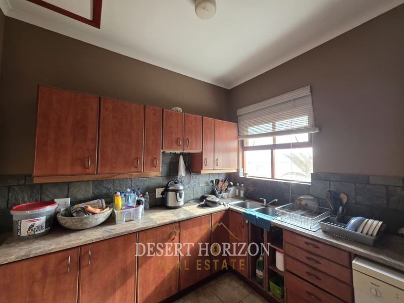 A functional kitchen featuring wooden cabinetry, laminate countertops, a double basin sink, and a tiled backsplash, offering a practical layout for daily use.