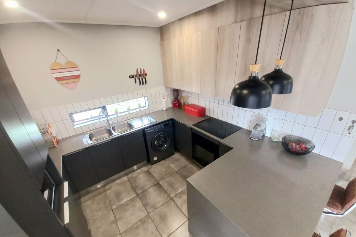 Modern kitchen featuring dark cabinetry, stone-look countertops, integrated hob and oven, double sink, and tiled flooring with contemporary pendant lighting.