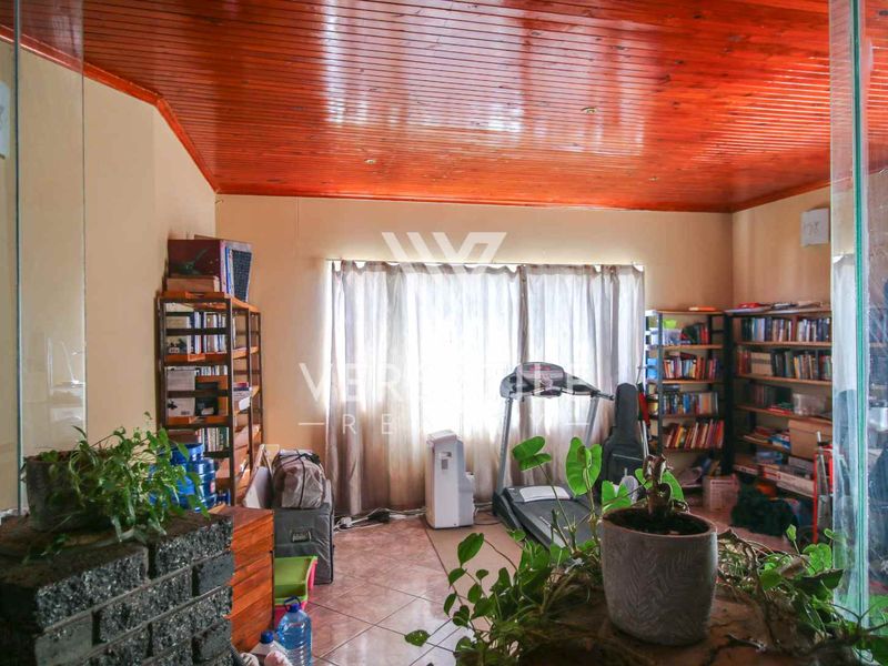 A living area featuring a warm timber tongue and groove ceiling, tiled flooring, and a glass partition wall, offering a versatile space.