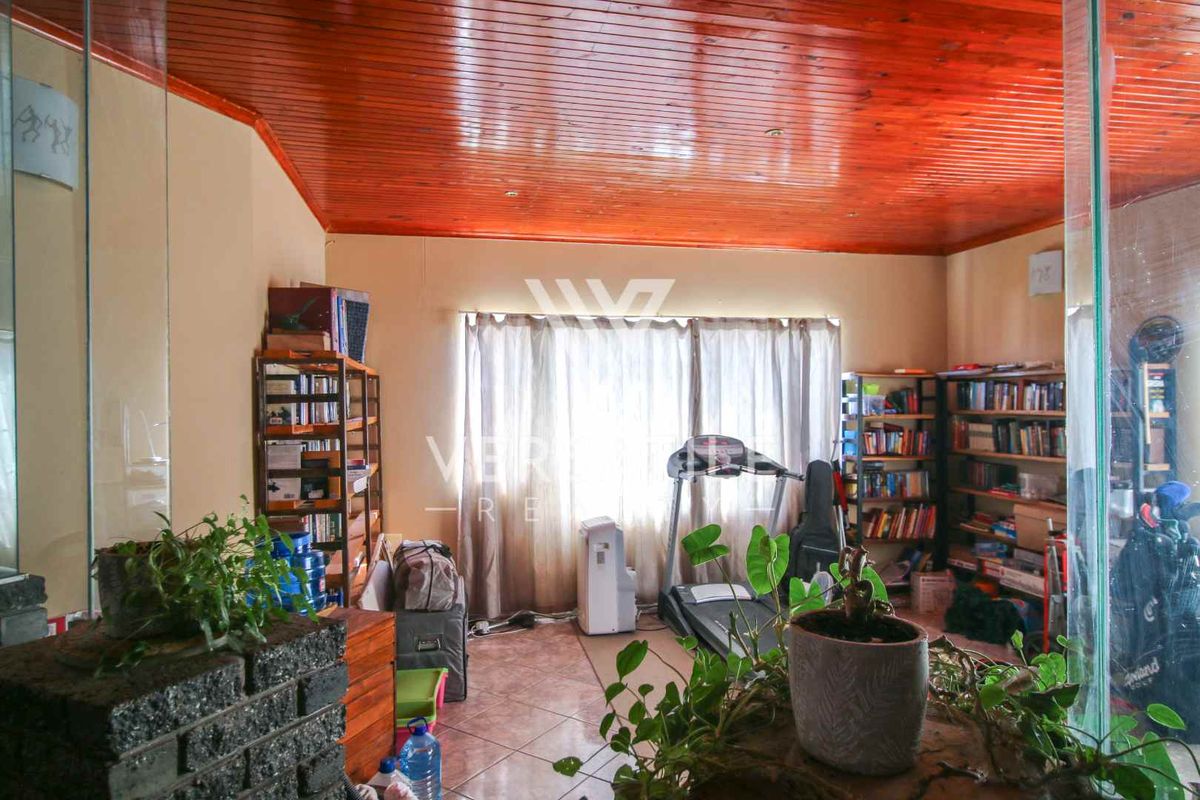 A living area featuring a warm timber tongue and groove ceiling, tiled flooring, and a glass partition wall, offering a versatile space.