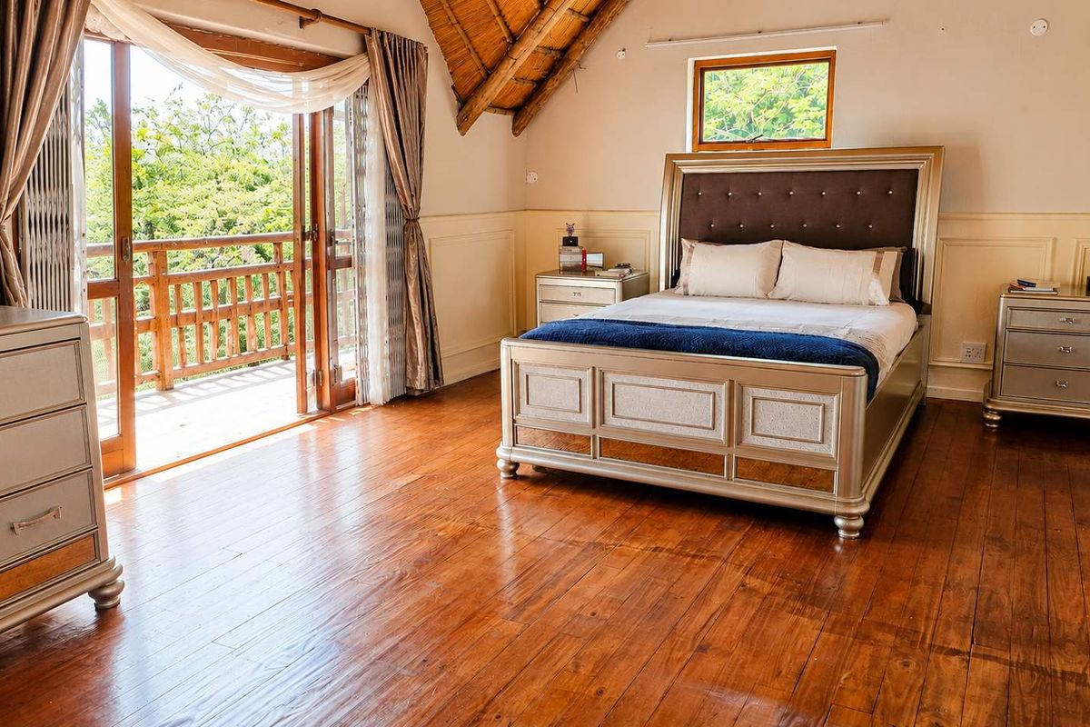 Spacious bedroom featuring warm hardwood flooring, a vaulted thatch ceiling, and direct access to a private balcony through wooden doors.